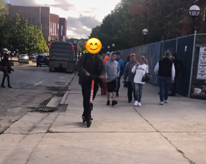 a person riding a rental scooter on the sidewalk on Central Campus.