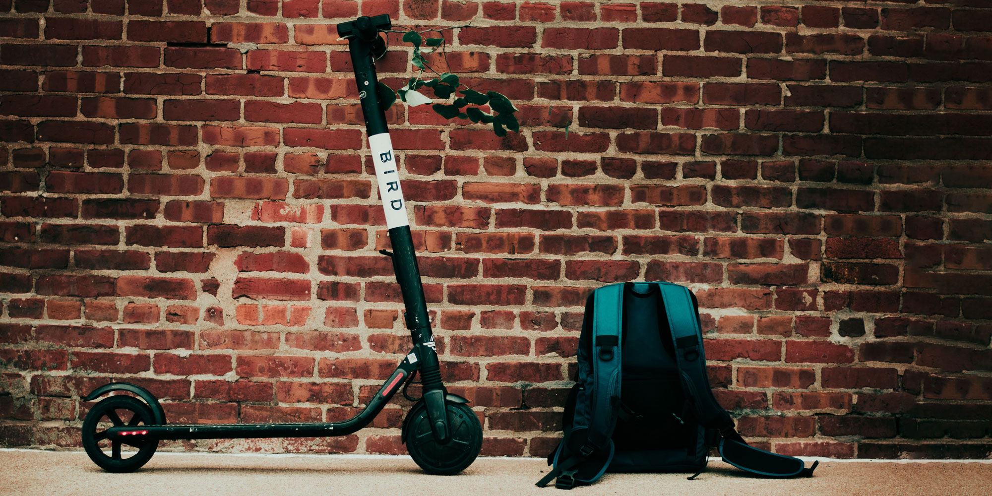 electric scooter and backpack against a brick wall